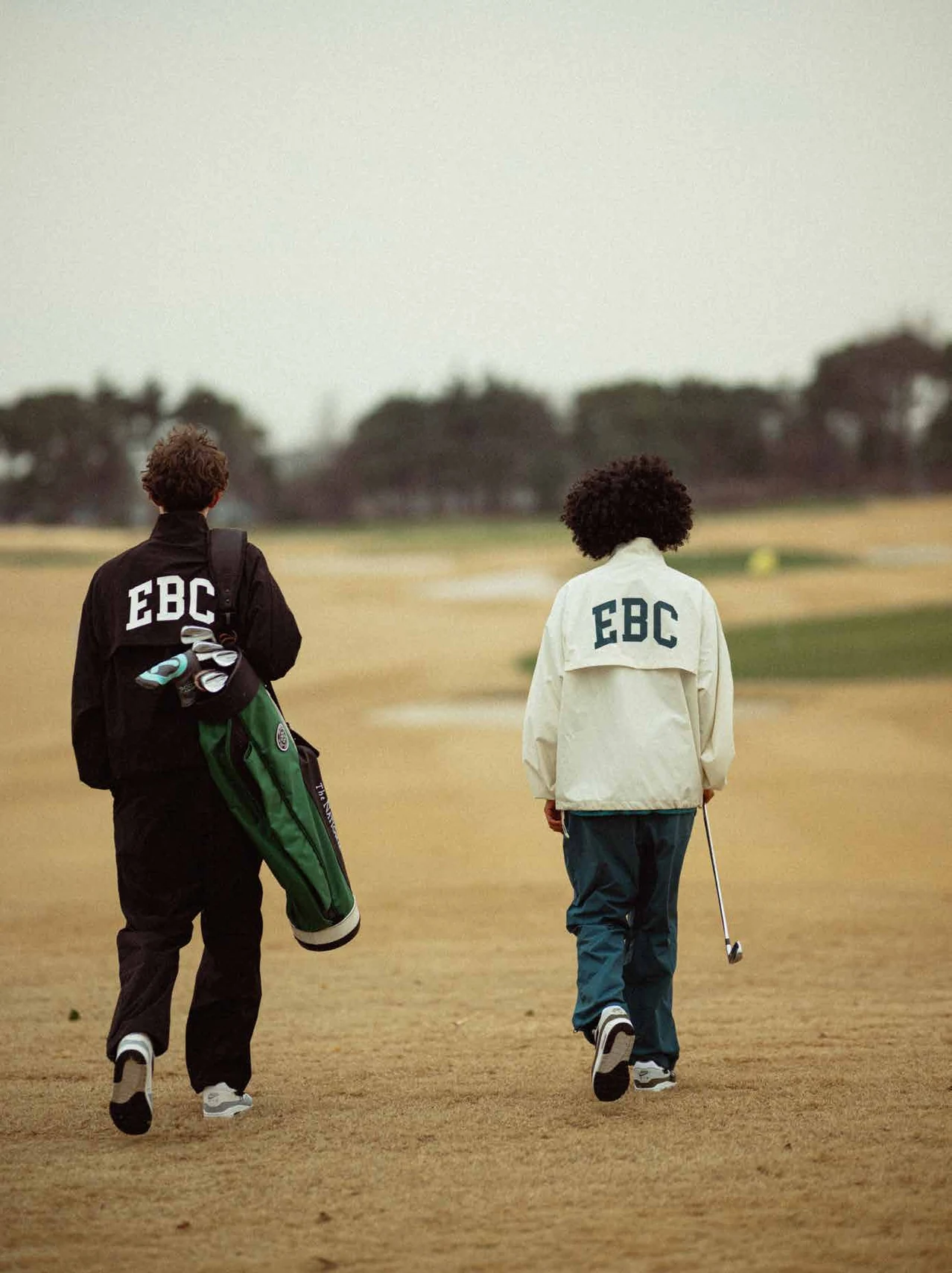 Two models in black and white Early Birds Club jackets on a golf course